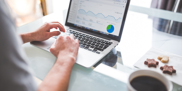 image of a person sitting in-front of a laptop with website metrics on the screen. cookies and a coffee cup are off to the side.